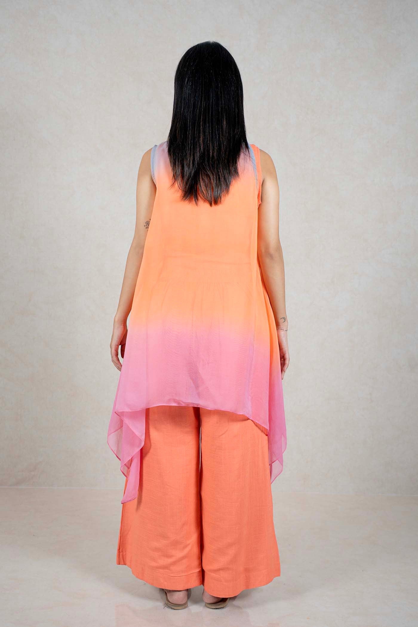 Back view of a woman wearing a Raysham Fashion orange sleeveless layered top and wide-leg trousers with a pink ombre shrug