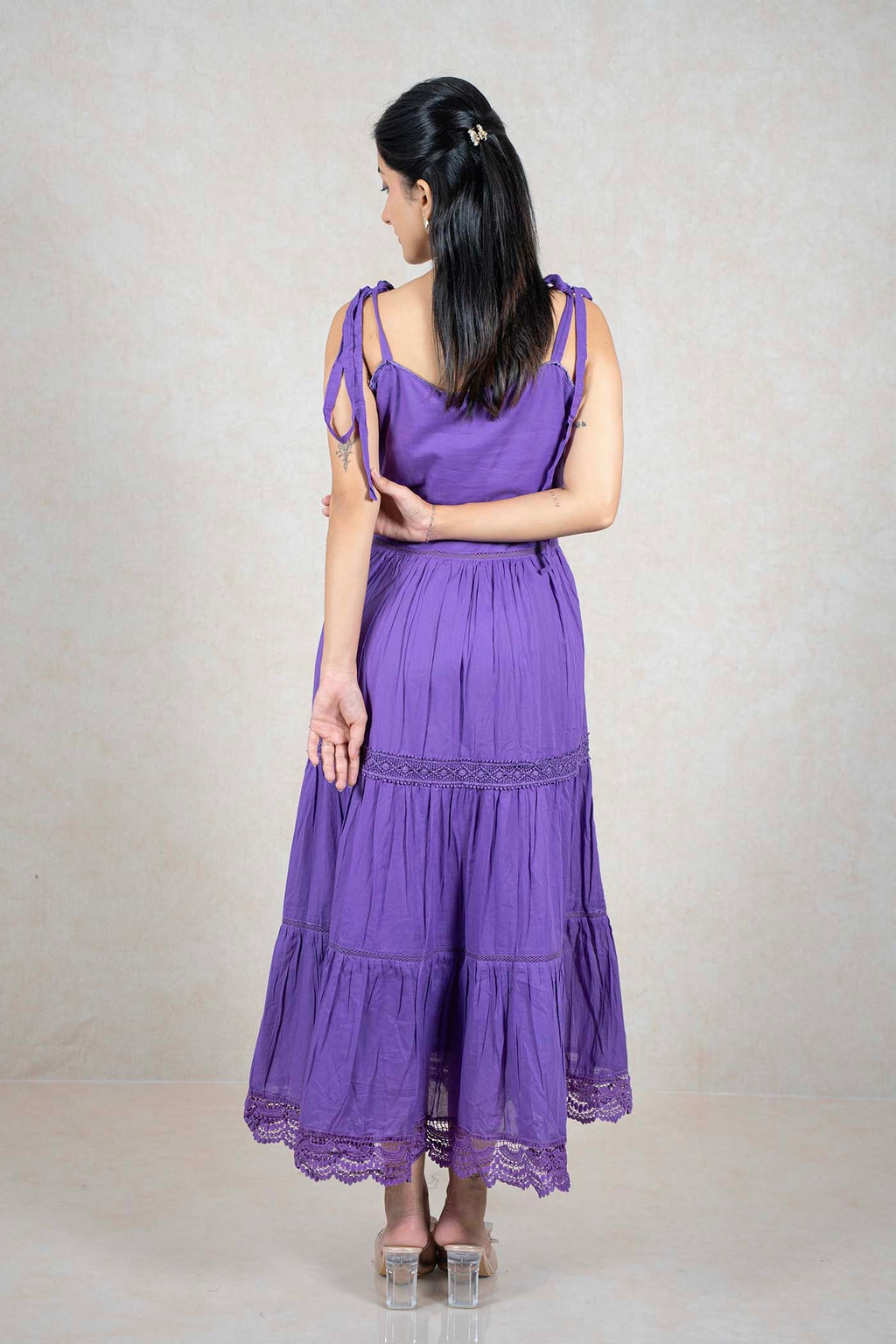 Back view of a woman wearing a Raysham Fashion purple tiered midi dress with lace trim and tie-up shoulder straps.