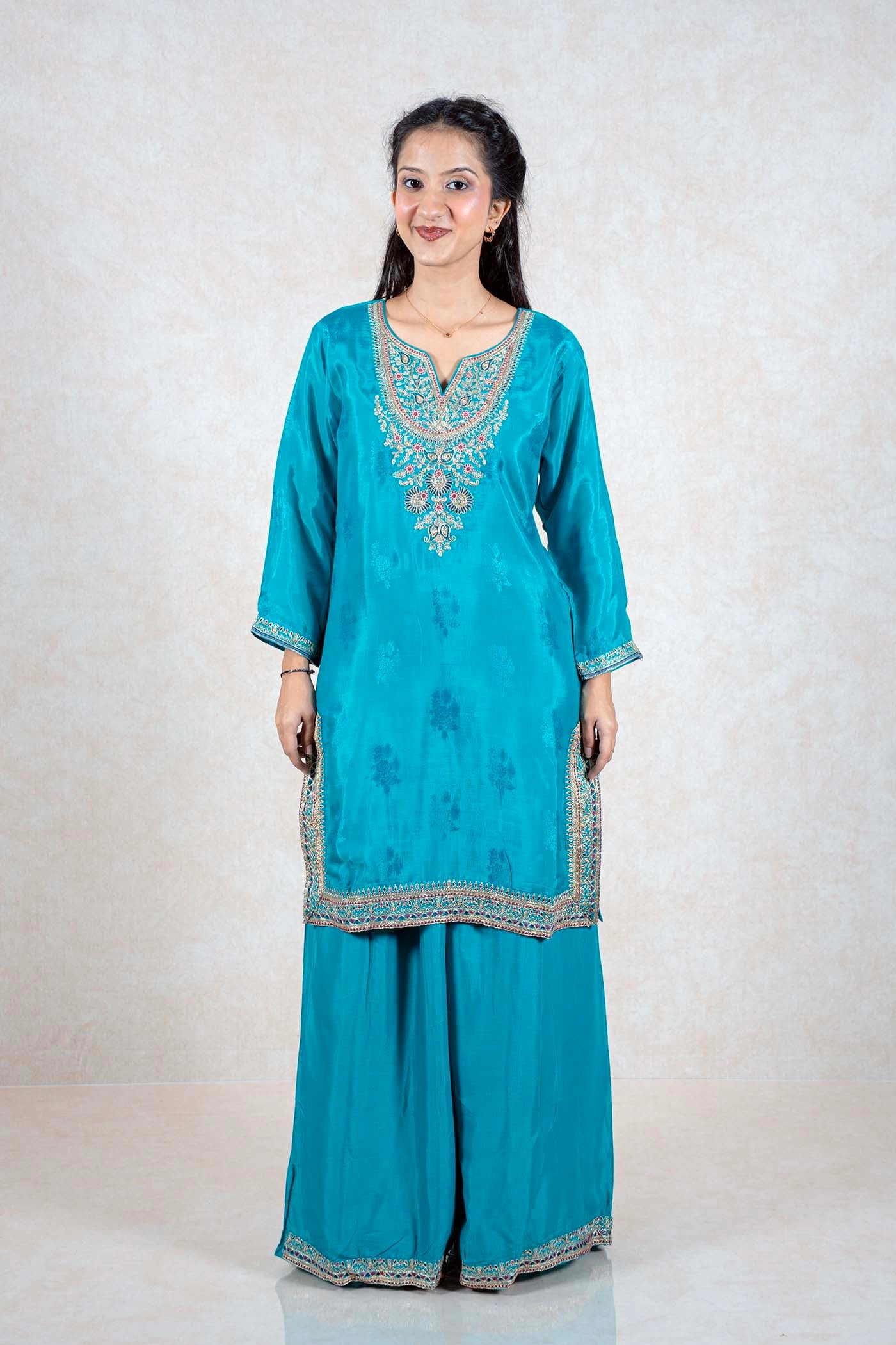Model wearing a teal Raysham Fashion silk kurta set with intricate multi-colored embroidery and wide-leg trousers.